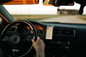 Vue conducteur de l'intérieur d'une voiture avec main sur le volant et smartphone GPS fixé au tableau de bord